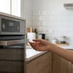 Persona apartando la mano del tirador de un horno empotrado por riesgo de calambre.