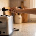 Por qué tu tostadora da corriente y qué hacer ya Mano desenchufando una tostadora de la pared en una cocina doméstica.